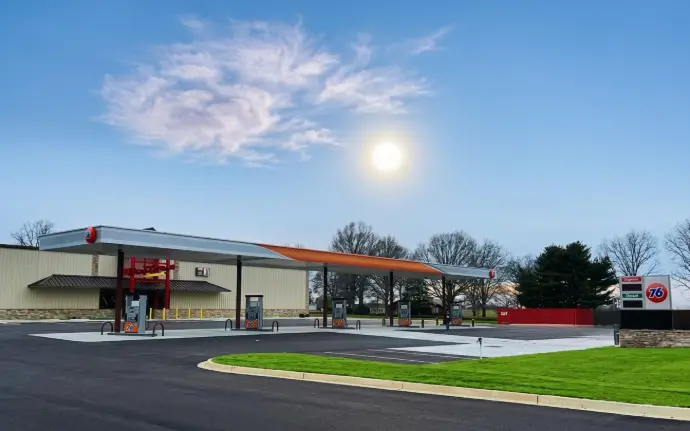 A modern 76 gas station under a bright sun and blue sky.
